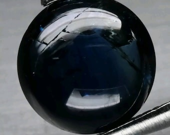May include: A dark blue round gemstone with a slight crack running through it. The gemstone is held in tweezers.
