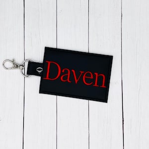 May include: Black leather keychain with a silver metal clasp and a red embroidered name tag that says "Daven".