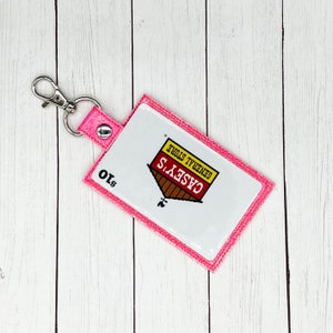 May include: Pink glitter keychain with a white Casey's General Store logo. The logo features a red roof and a yellow sign with the text "Casey's General Store". The keychain also has a silver metal ring and a $10 price tag.
