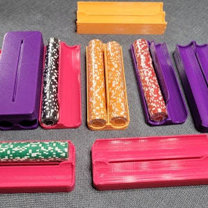 May include: A collection of colorful 3D-printed poker chip holders in various colors, including pink, purple, and orange. The holders are designed to hold stacks of poker chips, with some containing chips and others empty. The chips have white, red, green, and black designs.