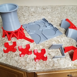 May include: A collection of 3D-printed components in gray and red, including a large funnel-shaped piece, a tray with circular cutouts, and several smaller support structures. The pieces are arranged on a speckled countertop.