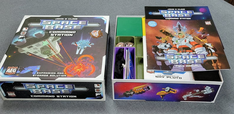 May include: A board game box set titled "Space Base Command Station" with a colourful outer box and an open inner box. The box art features spaceships and a fiery nebula. The set includes a field manual and game components.
