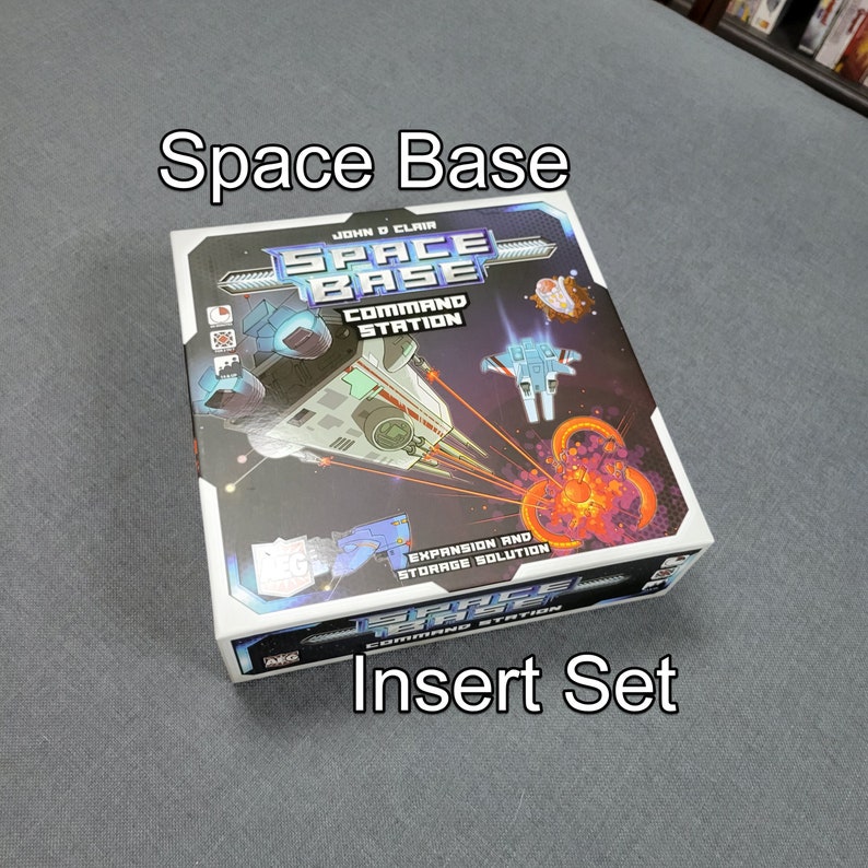 May include: A board game box labelled "Space Base" with a space theme. The box features illustrations of spaceships, planets, and the text "Command Station" and "Insert Set". The colour scheme includes blue, white, and orange.