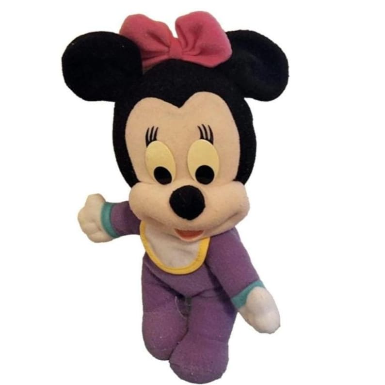 Pu&ograve; includere: Un peluche di un personaggio topo dei cartoni animati con orecchie nere, un fiocco rosa e un viso color crema. Il personaggio indossa un completo viola a maniche lunghe con una bavaglino bianco con bordo giallo e polsini color verde acqua.