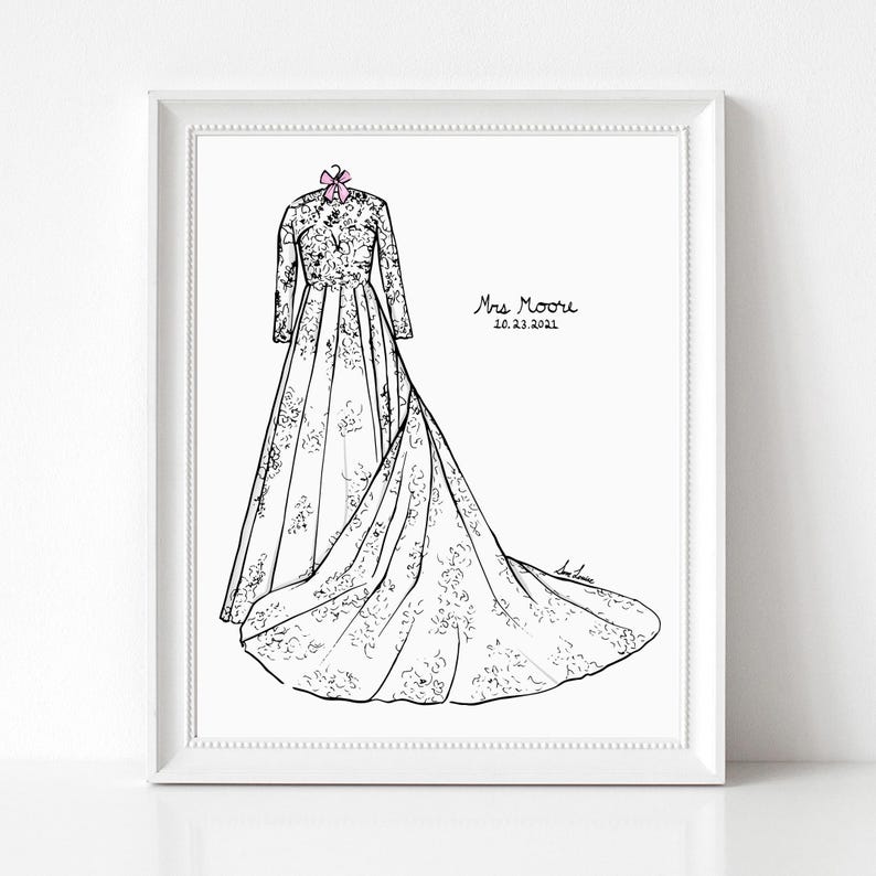 May include: A framed black and white line art illustration of a long-sleeved wedding dress with a floral pattern and a train, featuring a small pink bow at the neckline. The text Mrs Moore and 10.23.2021 are printed on the right side of the dress.