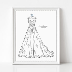 May include: A framed line art illustration of a floor-length wedding dress on a hanger with a blue bow. The hanger is labeled Mrs. The text Mrs. Abrantes and 06.04.2022 is printed to the right of the dress. The dress features intricate floral details.
