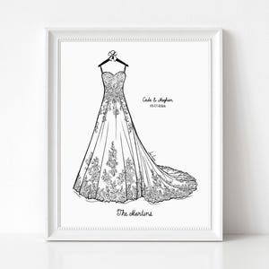 May include: A framed black and white line art illustration of a strapless wedding dress with a long train hanging on a hanger. The text reads Cade & Meghan 05.17.2026 and The Martins. The dress features intricate floral lace detailing.