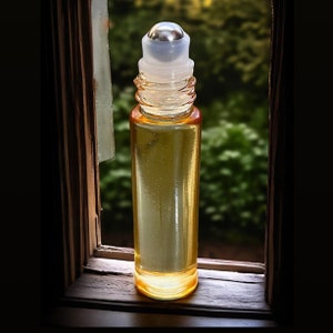 May include: A clear glass roller bottle with a silver metal roller ball and a yellow liquid inside. The bottle is sitting on a wooden surface.