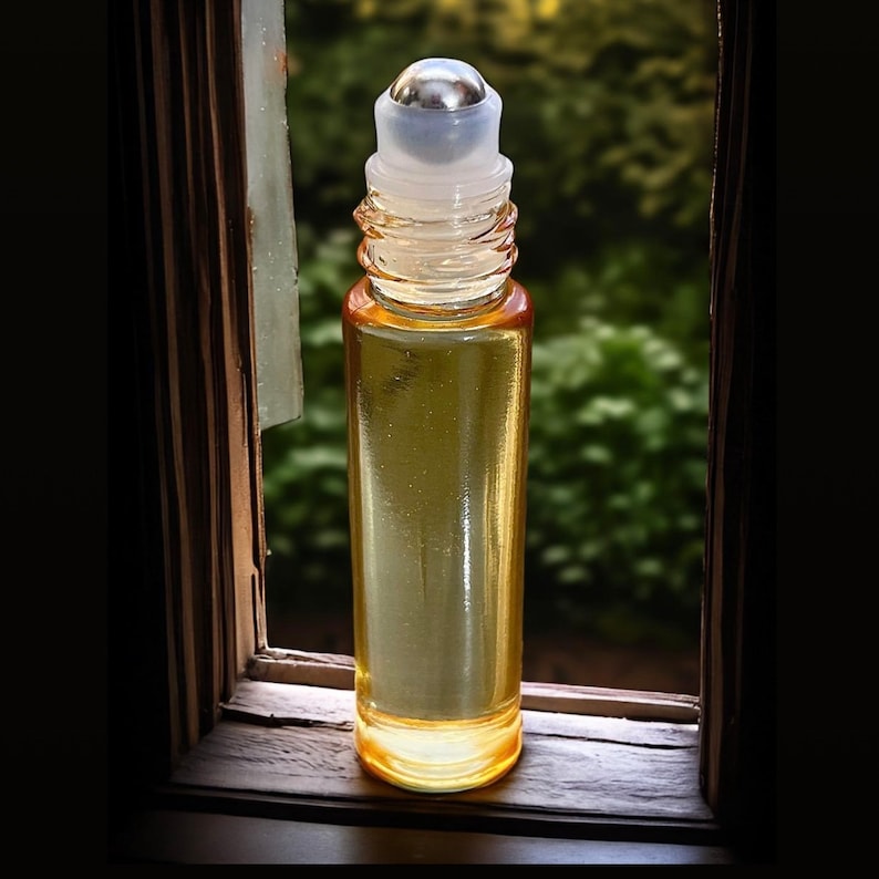 May include: A clear glass roller bottle with a silver metal roller ball and a yellow liquid inside. The bottle is sitting on a wooden surface.
