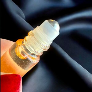 May include: A clear glass roller bottle with a gold liquid inside. The roller ball is clear and the bottle has a silver cap.