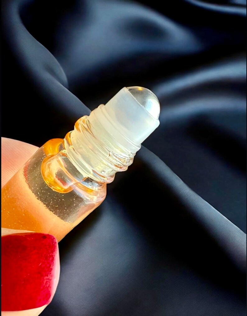 May include: A clear glass roller bottle with a gold liquid inside. The roller ball is clear and the bottle has a silver cap.