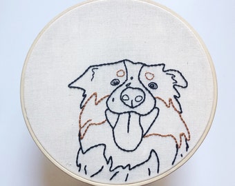 May include: Embroidered design of a dog's face on a white fabric stretched over a round wooden frame.