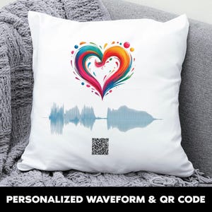 May include: White square pillow with a colorful heart design and a blue waveform graphic. The heart is a mix of rainbow colors. The pillow also features a QR code and the text "PERSONALIZED WAVEFORM & QR CODE" in black.