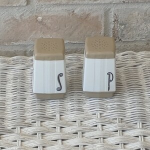 May include: Two white ceramic salt and pepper shakers with brown tops. The shakers have a vertical ribbed design and the letters "S" and "P" are printed on the front.