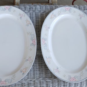 May include: Two oval serving platters with a floral design in shades of pink, gray, and green. The platters are white with a raised rim.