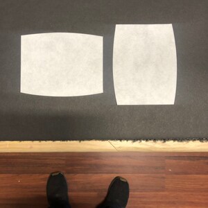 May include: Two white filter inserts for a face mask. The inserts are rectangular and curved at the top and bottom. The inserts are on a dark gray surface.
