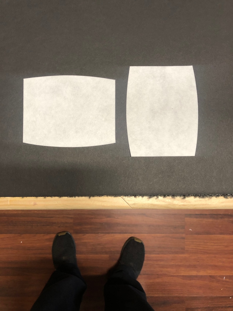 May include: Two white filter inserts for a face mask. The inserts are rectangular and curved at the top and bottom. The inserts are on a dark gray surface.