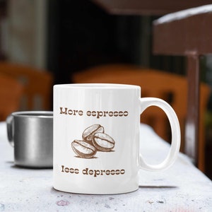 May include: White ceramic mug with a brown handle. The mug has brown text that reads "More espresso less depresso" and a drawing of three coffee beans.