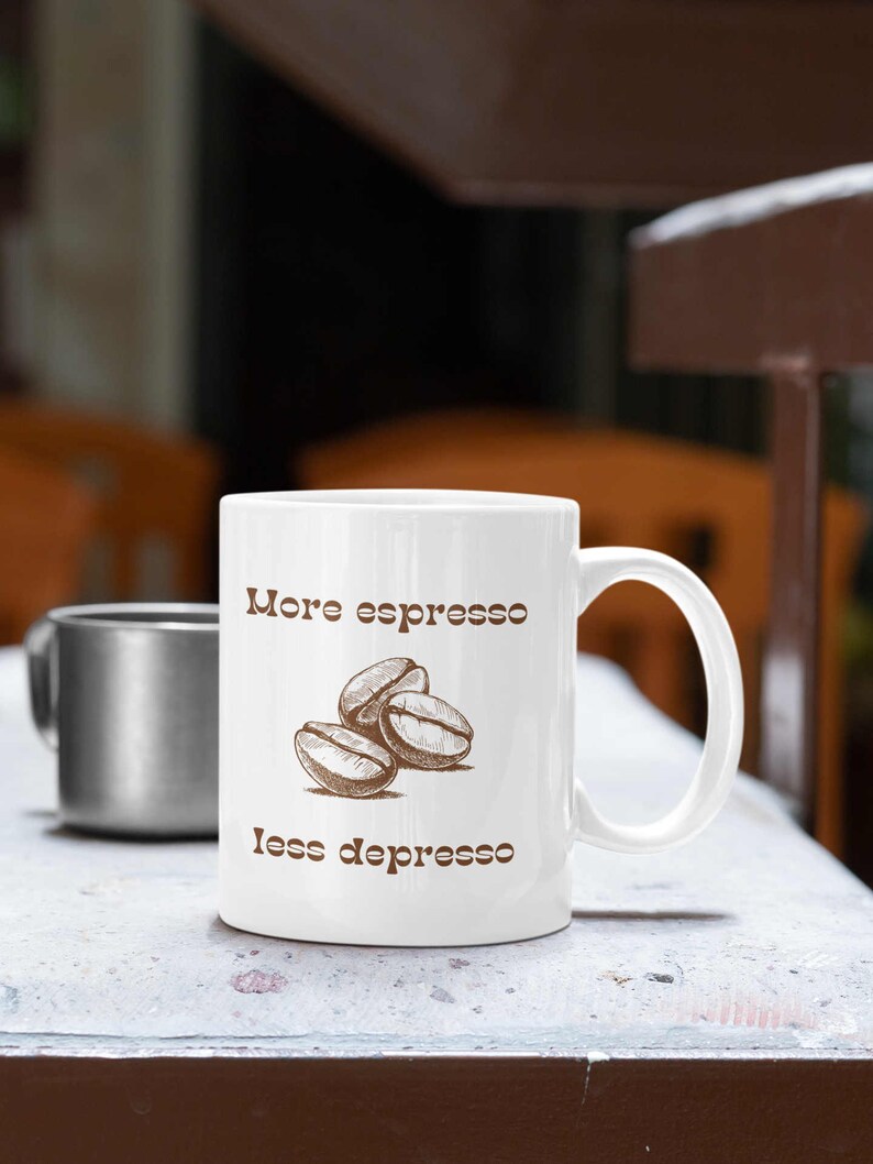 May include: White ceramic mug with a brown handle. The mug has brown text that reads "More espresso less depresso" and a drawing of three coffee beans.