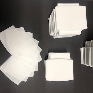 May include: A stack of white fabric squares, some are folded in a fan shape, others are stacked neatly. The fabric is likely for crafting or sewing projects.