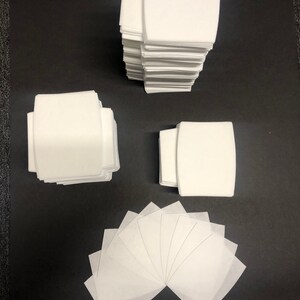 May include: A stack of white fabric squares, a stack of white fabric rectangles, and a fan of white fabric squares. The fabric squares and rectangles are all the same size and shape.