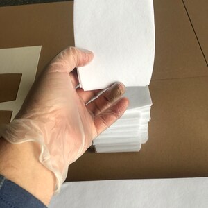May include: A stack of white paper sheets, approximately 100 sheets, are held in a gloved hand. The paper is smooth and appears to be high quality.