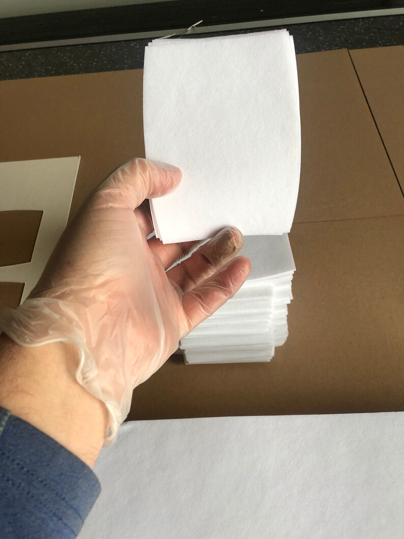 May include: A stack of white paper sheets, approximately 100 sheets, are held in a gloved hand. The paper is smooth and appears to be high quality.