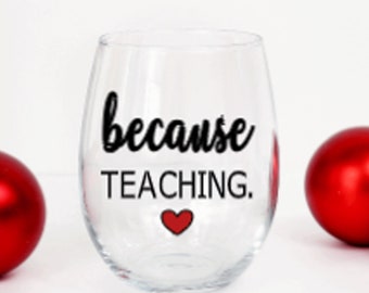 May include: A clear glass wine glass with the text "because teaching." in black lettering and a red heart.
