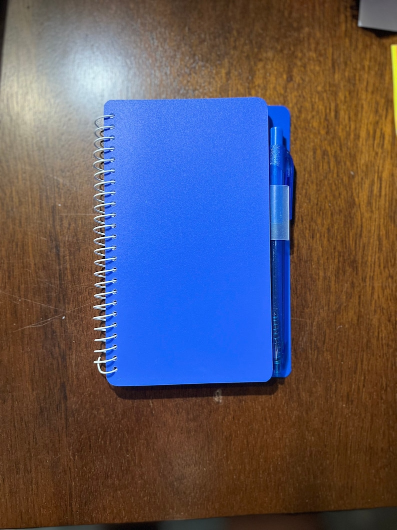 May include: A blue spiral bound notebook with a blue pen attached to the cover.