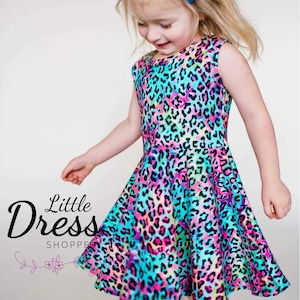 May include: A young girl wearing a sleeveless dress with a colorful leopard print. The dress has a fitted bodice and a flared skirt. The girl is wearing a blue bow in her hair.