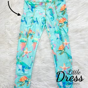 May include: Teal leggings with a sea life print featuring seahorses, whales, starfish, and turtles. The leggings have pockets on the sides.