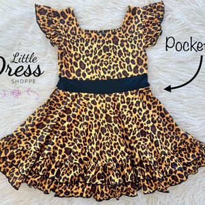 May include: A brown and yellow leopard print dress with black ruffle trim and a black waistband. The dress has short sleeves with ruffles and pockets on the sides.