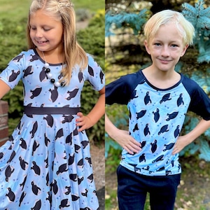 May include: Two children wearing blue and black shirts with a penguin pattern. The shirts have a light blue background with black penguins and white hearts. The girl is wearing a dress and the boy is wearing a short-sleeved shirt.
