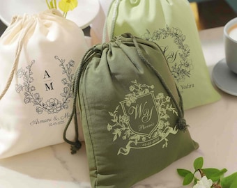 May include: Three drawstring bags with personalized floral designs and initials. The bags are made of natural fabric and are in white, light green, and dark green.