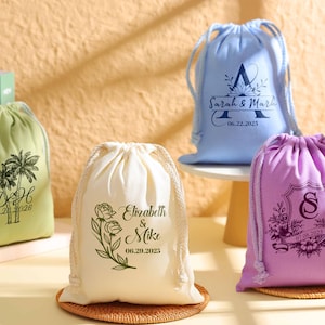 May include: Four personalized drawstring bags in different colors and designs. The bags are made of natural fabric and feature a variety of designs, including palm trees, flowers, and initials. The bags are perfect for wedding favors, party favors, or gifts.