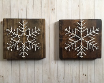 Peut inclure: Deux panneaux en bois avec des flocons de neige en fil blanc sur un fond en bois blanc.
