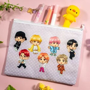 May include: A purple and white polka dot pencil case with a zipper closure. The case features seven cartoon characters with different hairstyles and clothing. The characters are all smiling and have different skin tones.