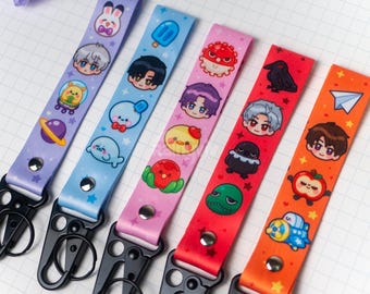 May include: A collection of five colorful lanyards with cartoon character designs. The lanyards are in purple, light blue, pink, red, and orange. Each lanyard has a black metal clasp and features various cute illustrations.