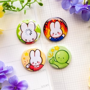 May include: Four circular pin-back buttons featuring cartoon characters. One shows a white rabbit with a loading icon, another a white rabbit surrounded by orange flames, a third a white rabbit giving a thumbs up, and the last a green character.