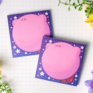 Puede incluir: Dos blocs de notas cuadrados con un personaje de dibujos animados rosa con un cuerpo redondo y brazos y pies pequeños. El personaje está sobre un fondo morado con estrellas blancas. Los blocs de notas están sobre un fondo de cuadrícula blanca.