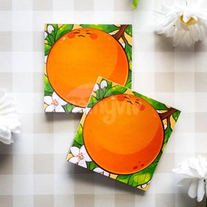 May include: Two square orange-themed stickers with a cartoon orange design. The oranges have a smiling face and are surrounded by green leaves and white flowers. The stickers are on a checkered background.