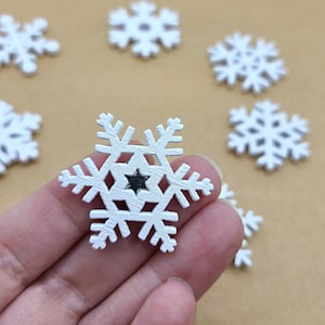 May include: White wooden snowflake ornaments with a star-shaped cutout in the center. The snowflakes have a rustic, textured appearance and are scattered on a light brown surface. These decorative ornaments are ideal for winter or holiday crafts.