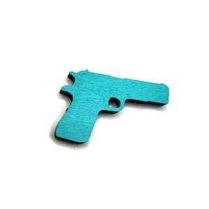 May include: A turquoise wooden pistol cutout, set against a white background. The toy gun is a detailed silhouette, showcasing the shape of a handgun. The wood grain is visible, adding texture to the solid color.