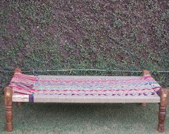 May include: A traditional Indian bed frame with a woven fabric mattress. The bed is made of wood and has a natural finish. The fabric is a colorful pattern of red, blue, green, and yellow.