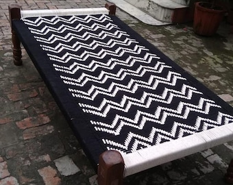 May include: A black and white patterned divan bed with wooden legs. The bed is made of woven rope and has a geometric design.