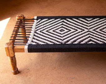 May include: A wooden bench with a black and white diamond patterned woven seat.