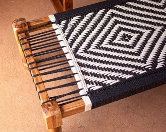 May include: A wooden bed frame with a black and white woven rope mattress. The frame has four legs and is made of dark wood.