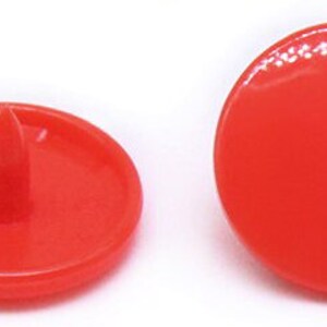 Peut inclure: Quatre boutons-pression en plastique rouge. Les boutons sont ronds et ont un dessus plat. Deux des boutons ont un centre sur&eacute;lev&eacute; et deux des boutons ont un centre plat.