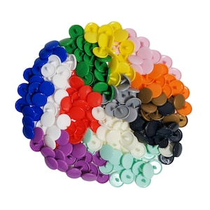 Peut inclure: Assortiment de boutons-pression en plastique de diff&eacute;rentes couleurs, dont le blanc, le rouge, l'orange, le jaune, le vert, le bleu, le violet, le marron, le noir et le gris. Les boutons sont dispos&eacute;s en cercle.