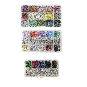 May include: A set of colorful metal snap fasteners in a clear plastic storage box. The box is divided into multiple compartments, each containing a different color of fasteners. The fasteners are small and round, with a metal ring around the center.
